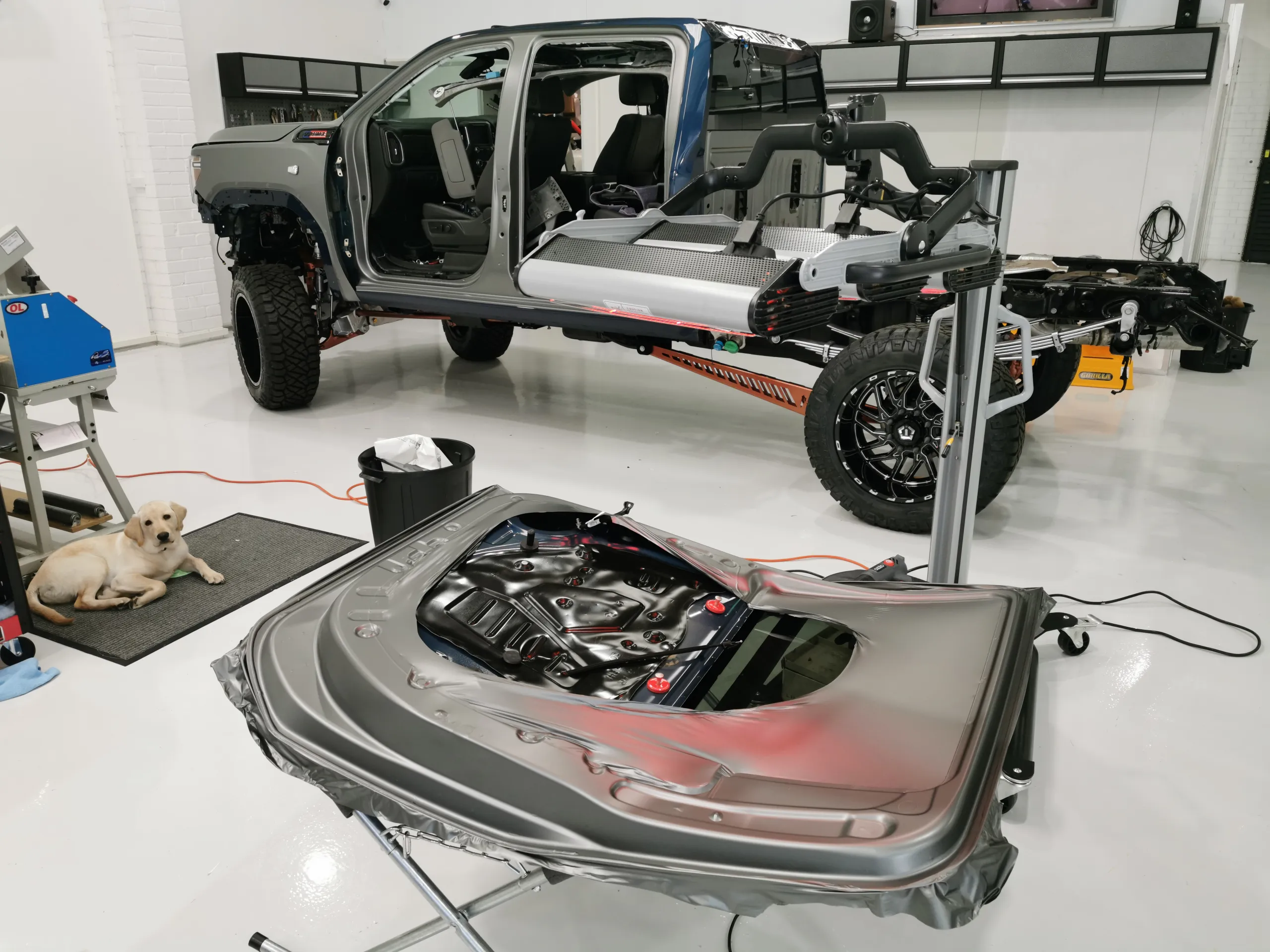 Dismantled ute cab and removed door on a workshop stand, with a dog nearby
