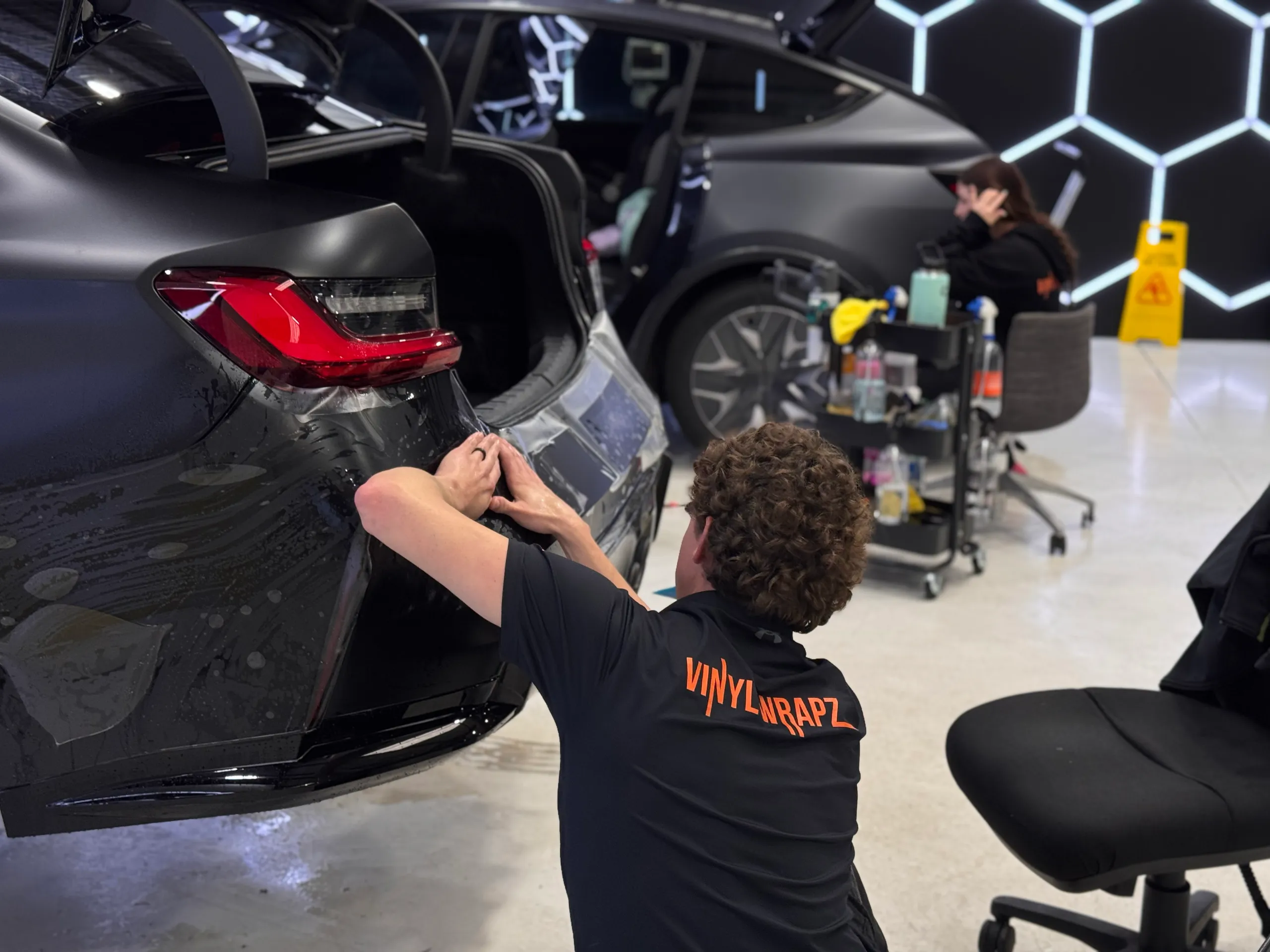 Installer fitting wet film around a car rear bumper with the boot open