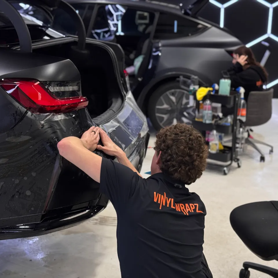 Installer fitting wet film around a car rear bumper with the boot open