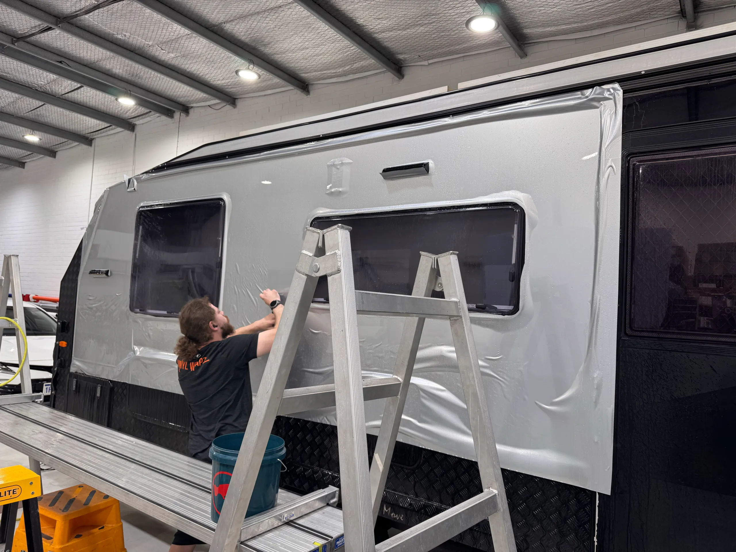 Installer fitting pale film around the windows of a caravan