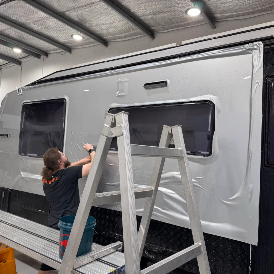 Installer fitting pale film around the windows of a caravan