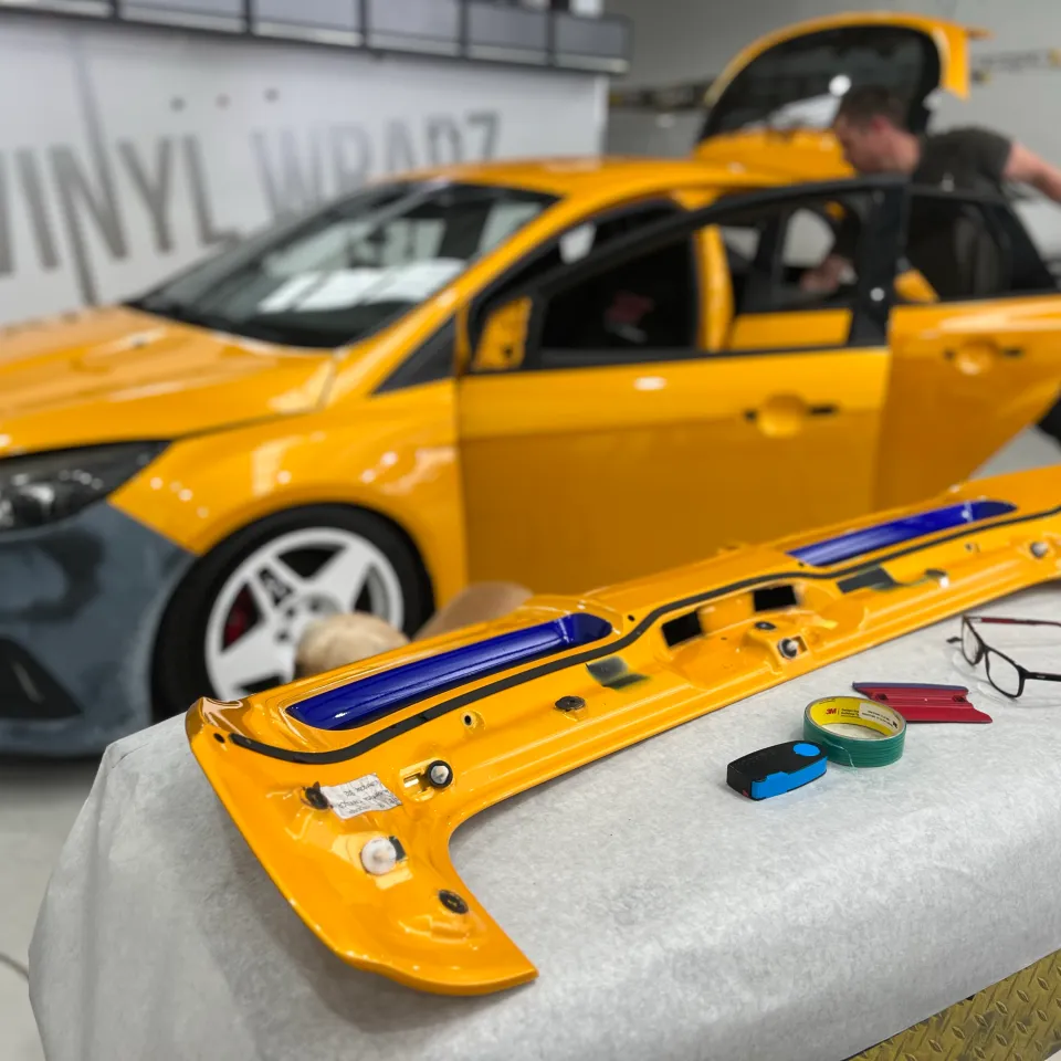 Yellow hatchback door removed for wrapping with an installer working beside the car