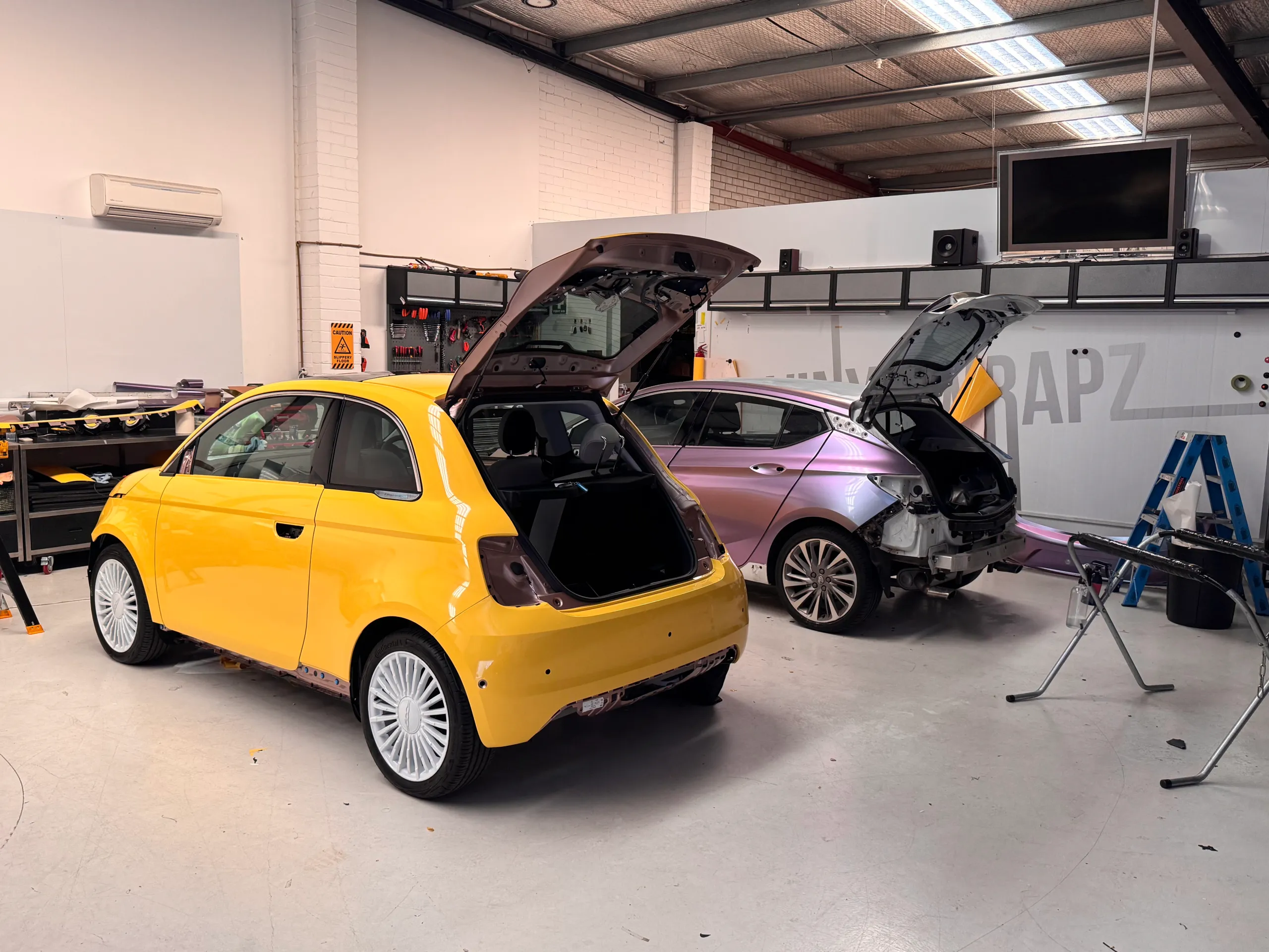 Yellow Fiat 500e and colour-shift Holden Astra with rear trim removed