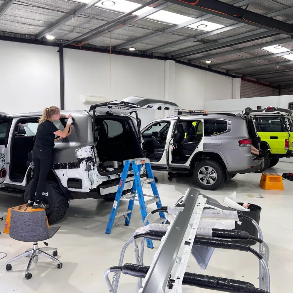 Installers applying grey film to dismantled LandCruisers in the workshop