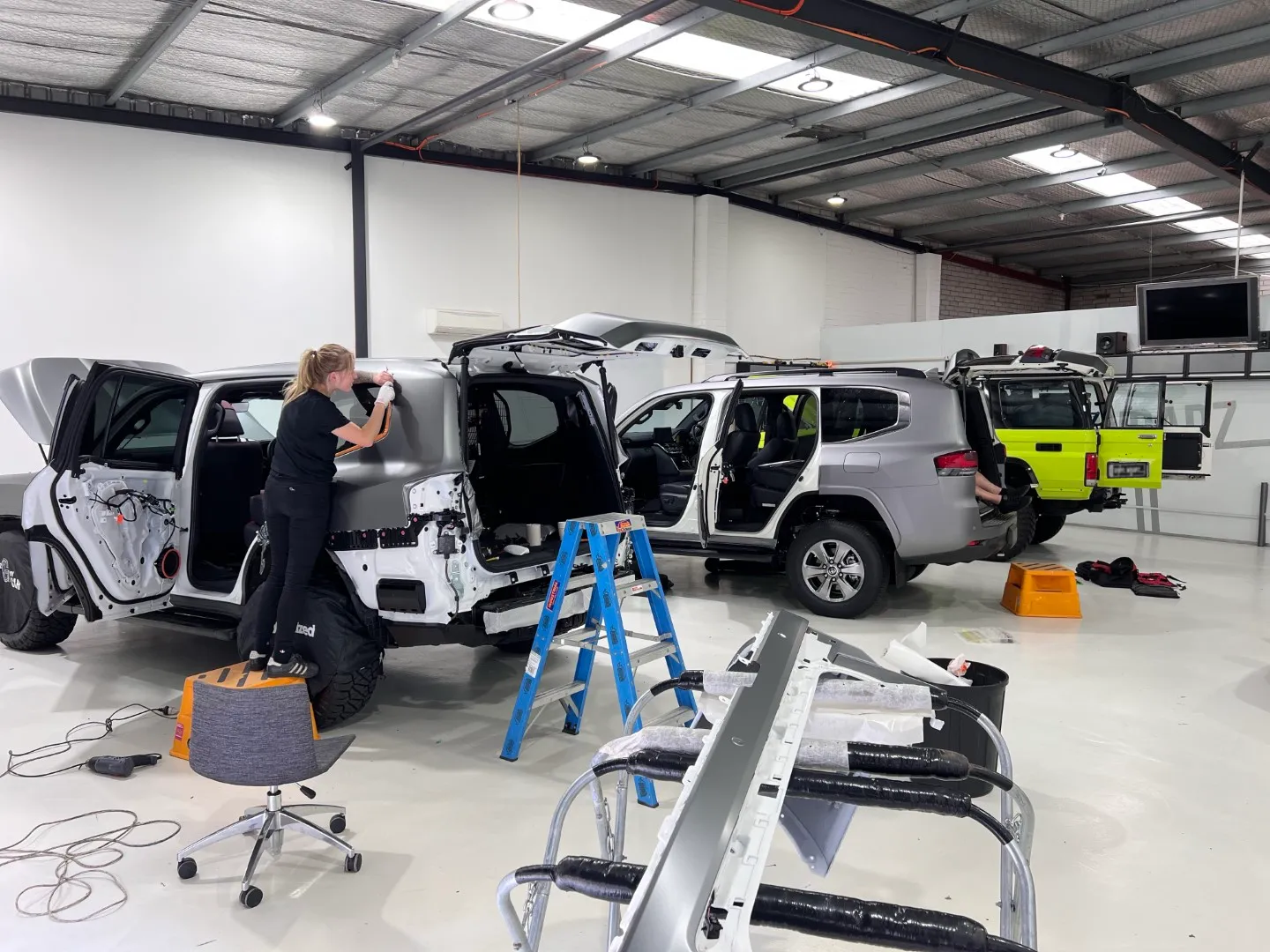 Installers applying grey film to dismantled LandCruisers in the workshop