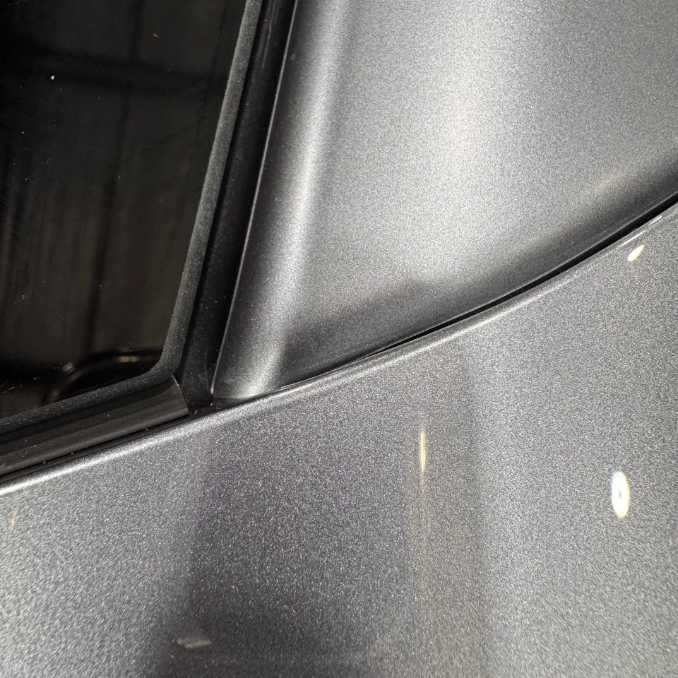 Grey wrapped pillar and adjoining body panel beside black window trim