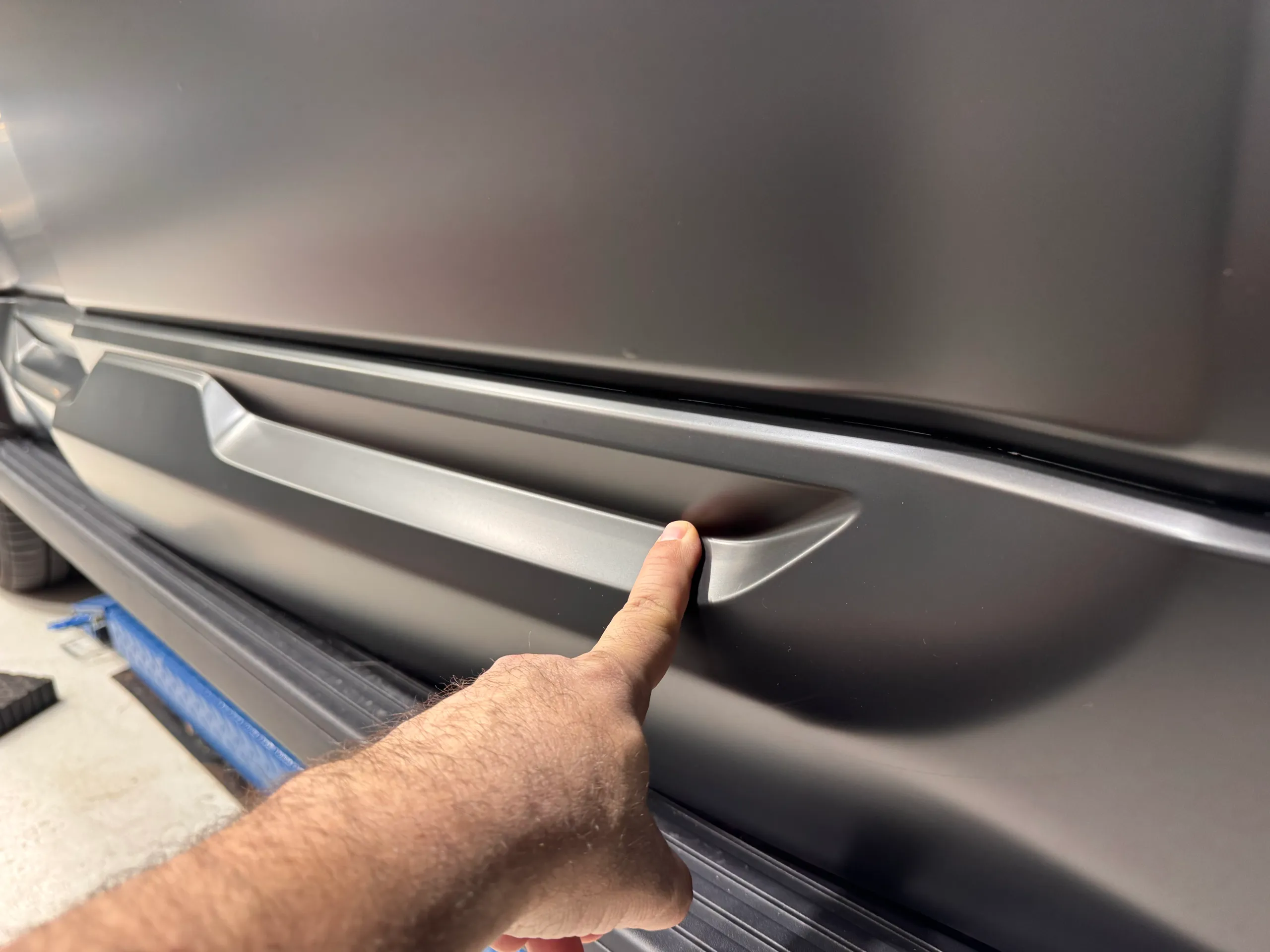 A hand indicating the recessed detail in a grey lower door moulding above a side step