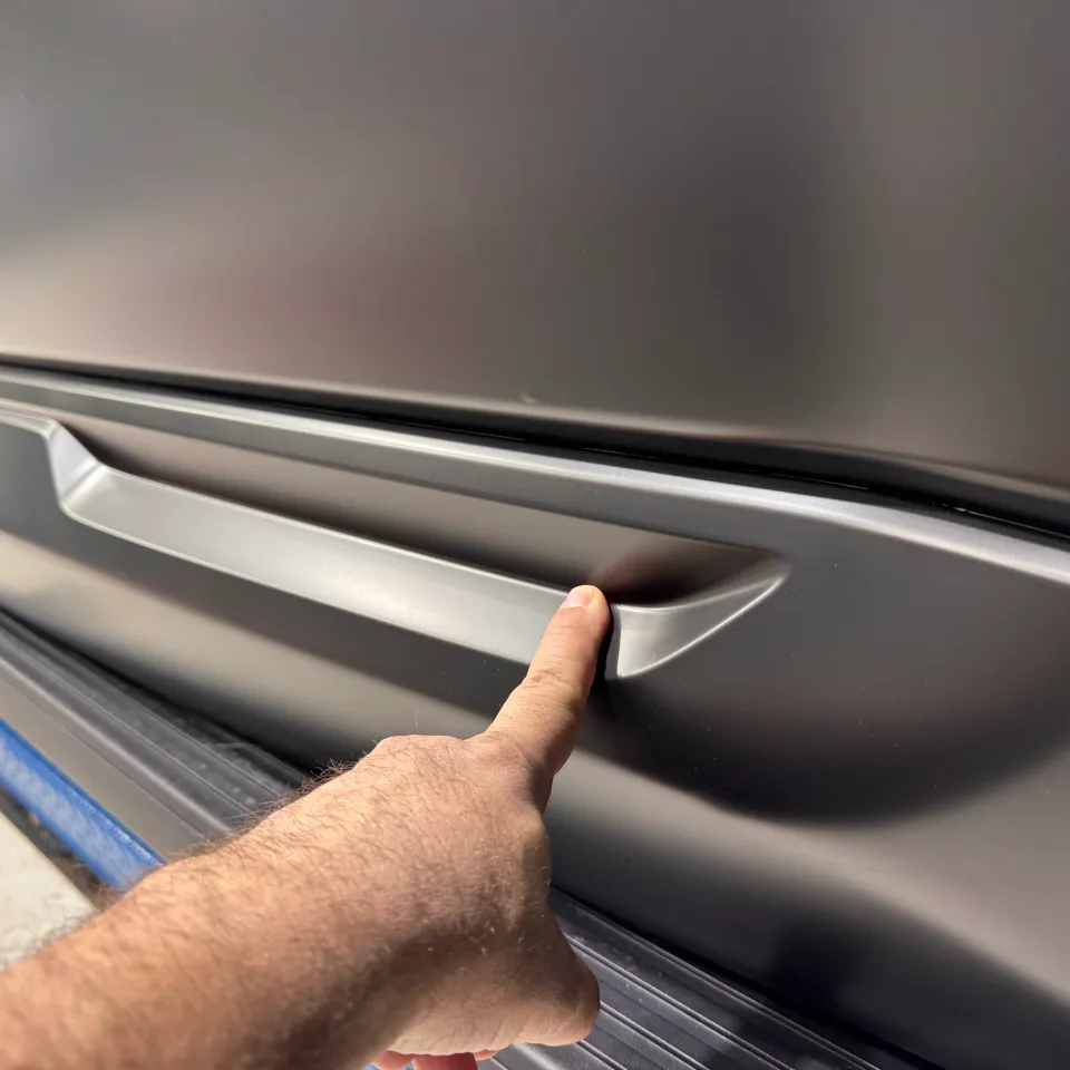 A hand indicating the recessed detail in a grey lower door moulding above a side step