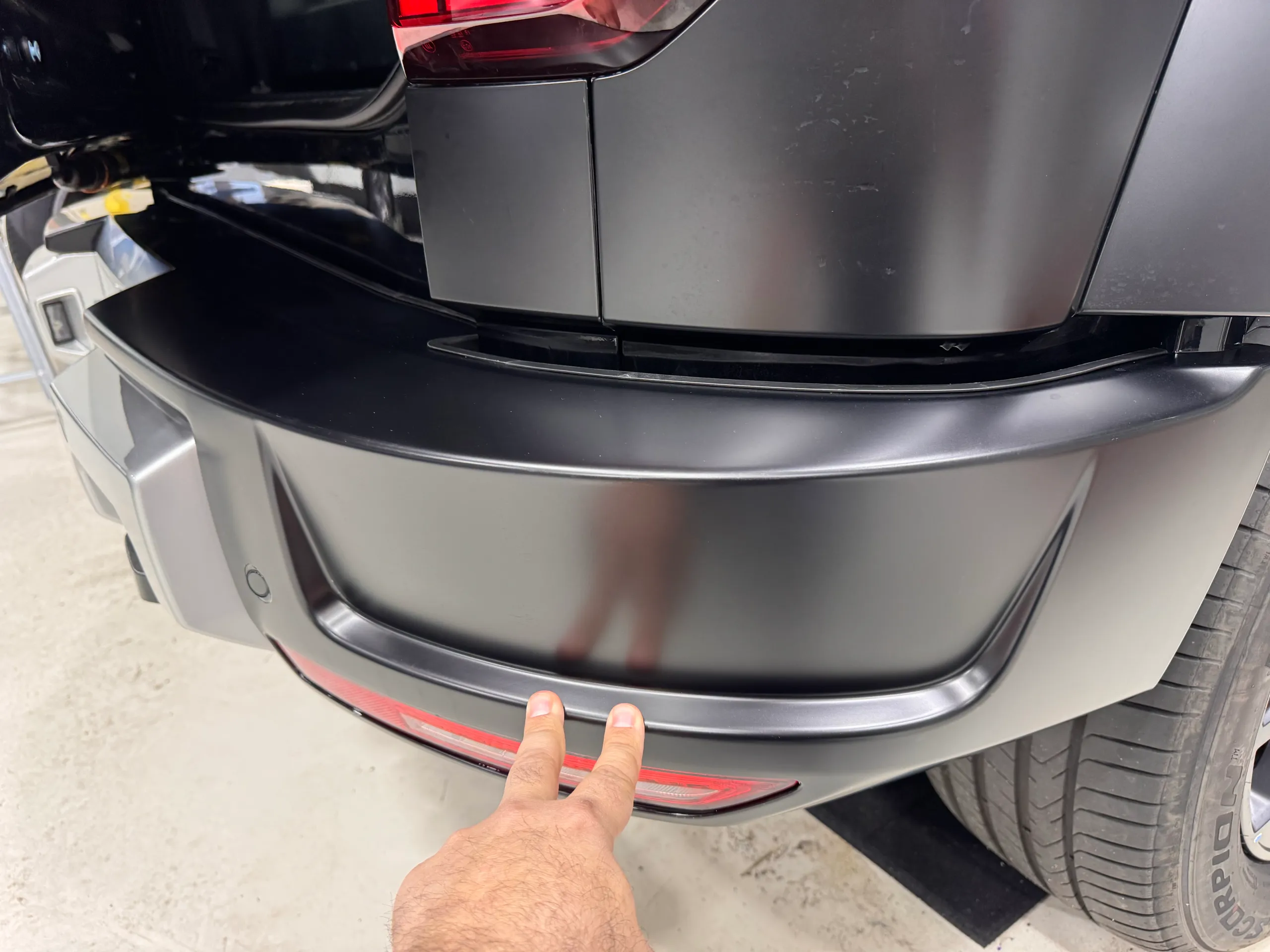 Two fingers indicating the lower edge of a grey rear bumper above its red reflector