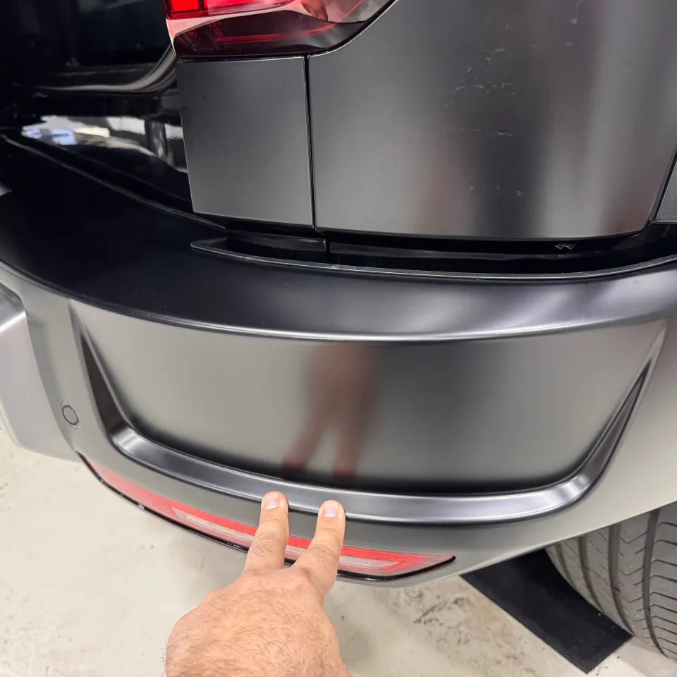 Two fingers indicating the lower edge of a grey rear bumper above its red reflector