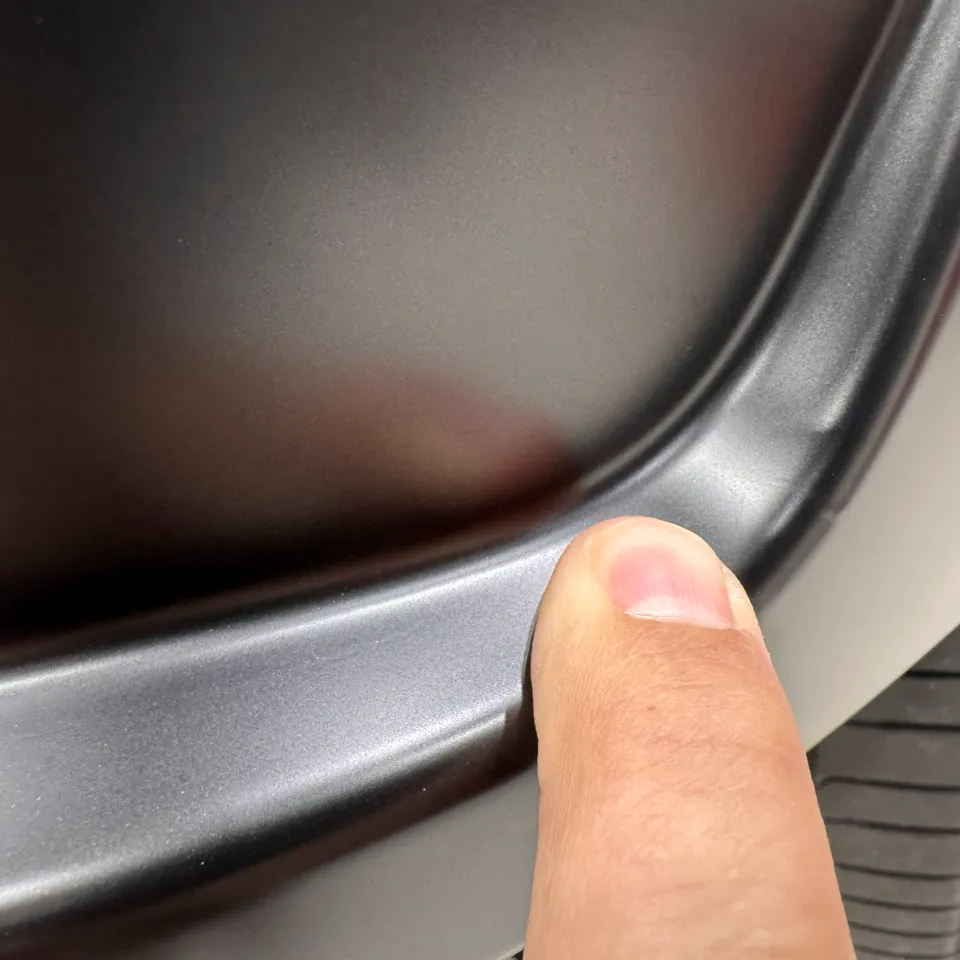 Close view of a fingertip beside a grey wrapped bumper trim edge