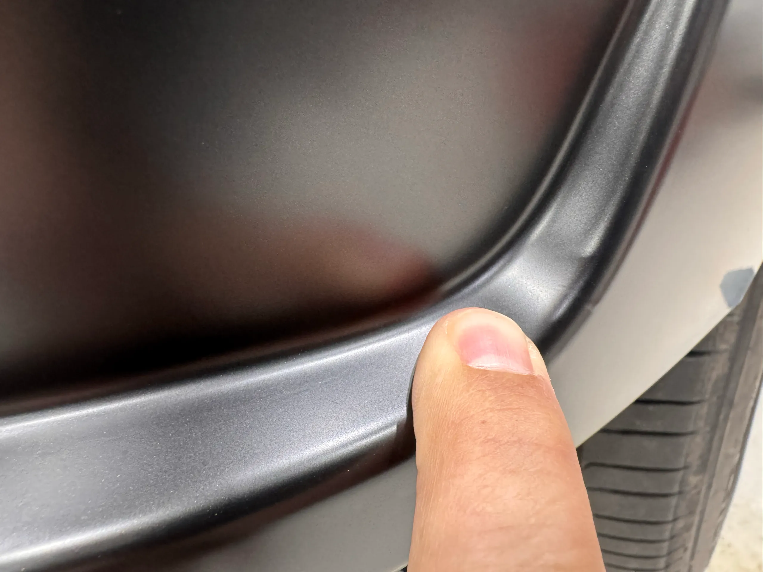 Close view of a fingertip beside a grey wrapped bumper trim edge