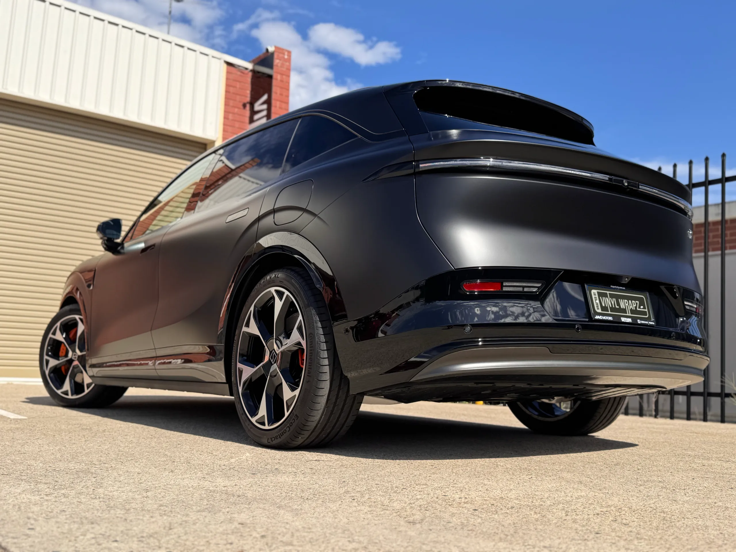 Low rear-quarter view of the satin black Zeekr 7X outside the workshop